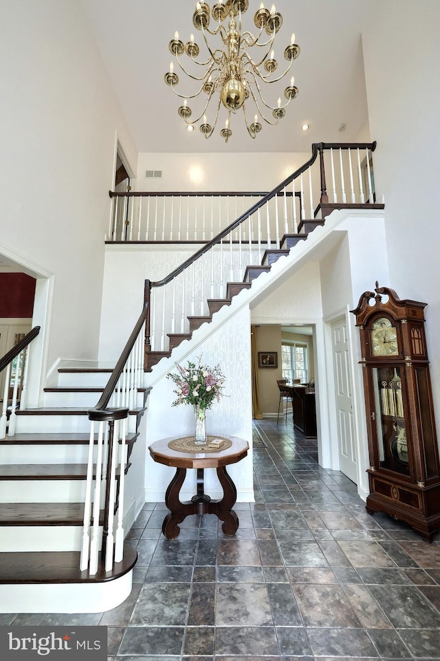 staircase featuring an inviting chandelier, a towering ceiling, stone tile flooring, and baseboards