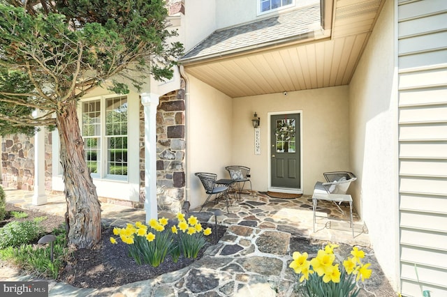 property entrance featuring stucco siding, covered porch, and stone siding