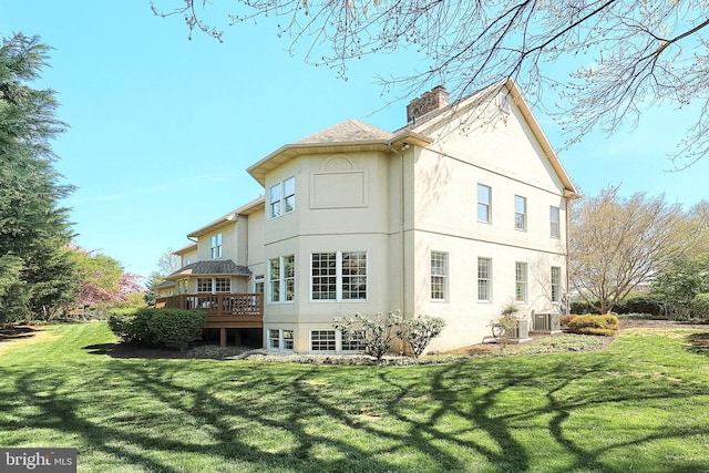 back of property with central air condition unit, a lawn, a chimney, a deck, and stucco siding