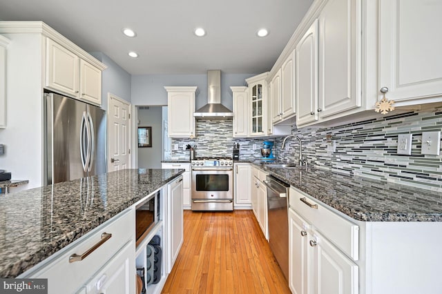 kitchen with wall chimney range hood, a sink, white cabinets, appliances with stainless steel finishes, and recessed lighting