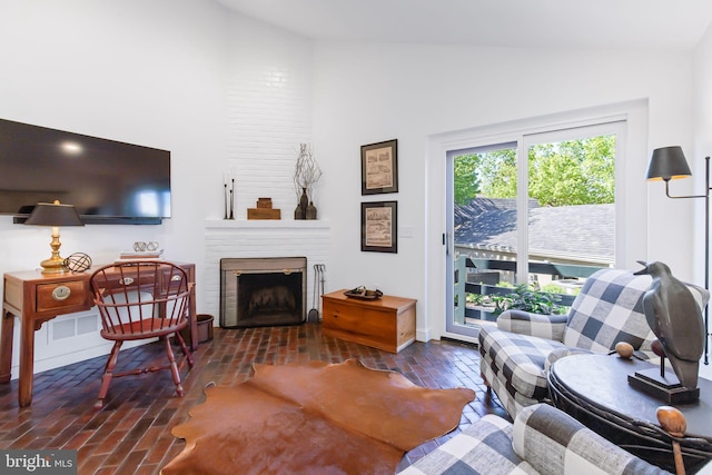 living area with brick floor, a fireplace, and high vaulted ceiling