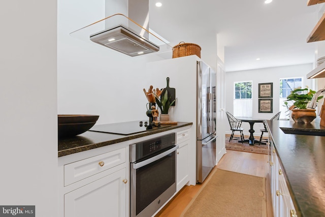 kitchen with light wood finished floors, stainless steel oven, island exhaust hood, white cabinetry, and dark countertops