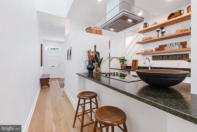 kitchen with open shelves, light wood-type flooring, a kitchen bar, range hood, and black electric cooktop