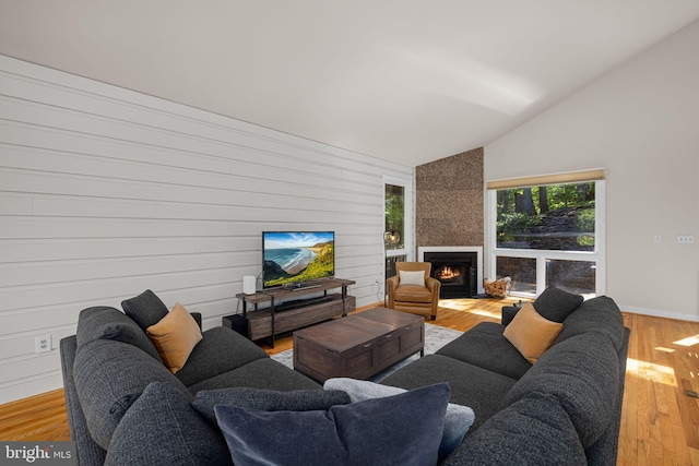 living room with wood finished floors, baseboards, lofted ceiling, and a large fireplace