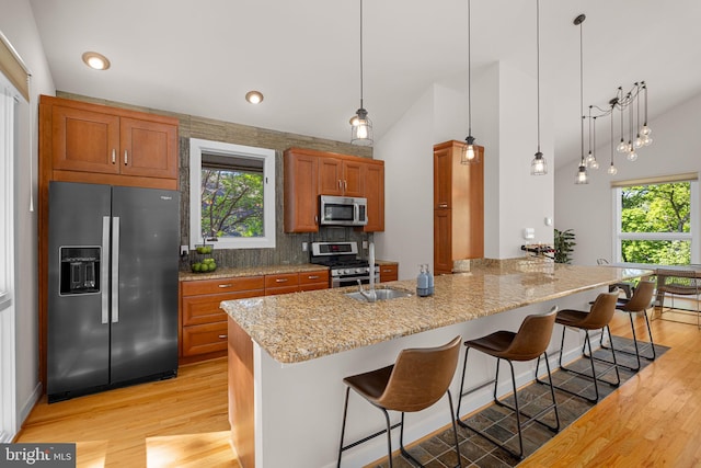kitchen with light wood-style floors, appliances with stainless steel finishes, brown cabinetry, and a breakfast bar area