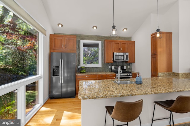 kitchen featuring a peninsula, appliances with stainless steel finishes, brown cabinetry, and lofted ceiling