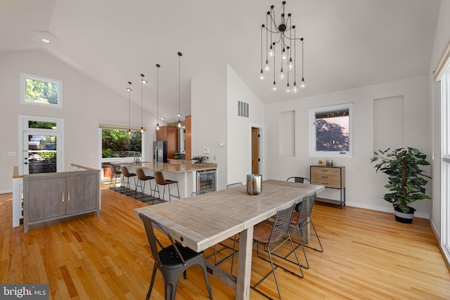 dining room featuring wine cooler, high vaulted ceiling, light wood-type flooring, and visible vents