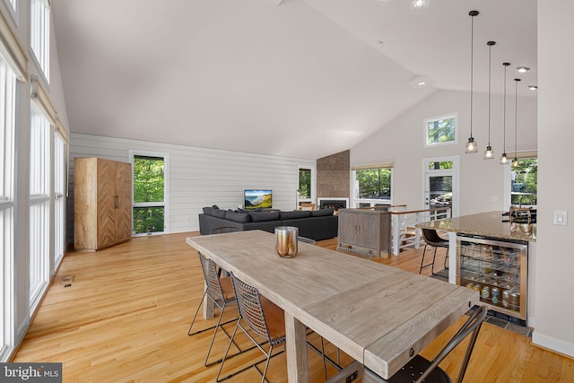 dining area with wine cooler, a large fireplace, light wood-style flooring, and a wealth of natural light