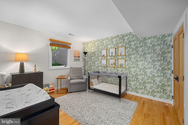 bedroom featuring wallpapered walls, visible vents, baseboards, and wood finished floors