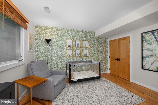living area with visible vents, wood finished floors, baseboards, an accent wall, and wallpapered walls