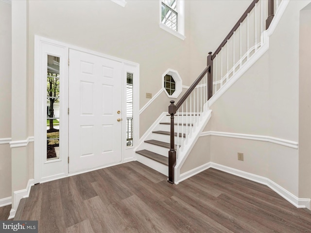 foyer entrance with baseboards, wood finished floors, a high ceiling, and stairway