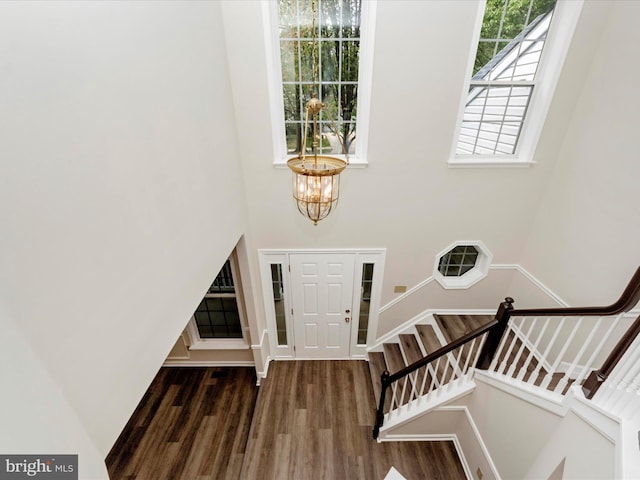 entryway with stairway, a towering ceiling, a chandelier, and wood finished floors