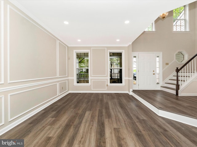 foyer entrance with recessed lighting, wood finished floors, ornamental molding, a decorative wall, and stairs