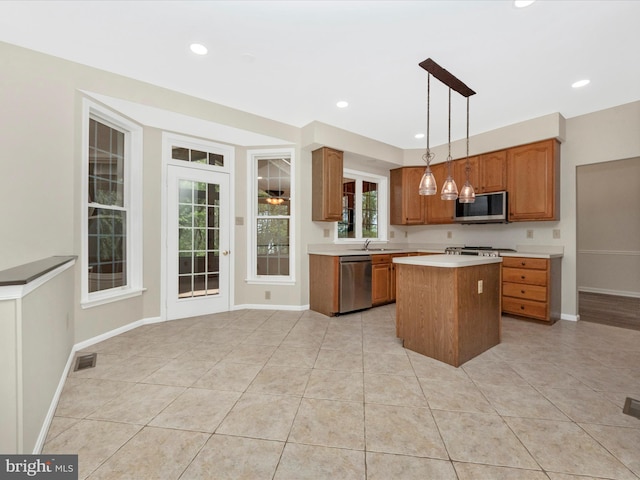 kitchen featuring brown cabinets, stainless steel appliances, light countertops, a sink, and a kitchen island