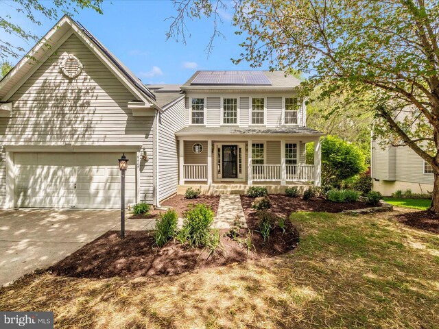 traditional-style home featuring solar panels, an attached garage, covered porch, and concrete driveway