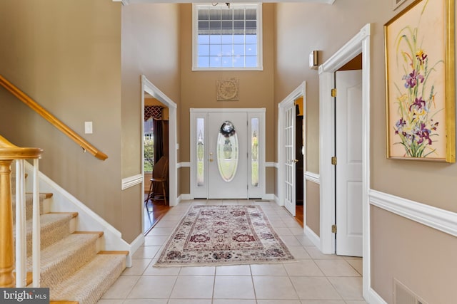 foyer featuring visible vents, stairway, tile patterned floors, baseboards, and a high ceiling