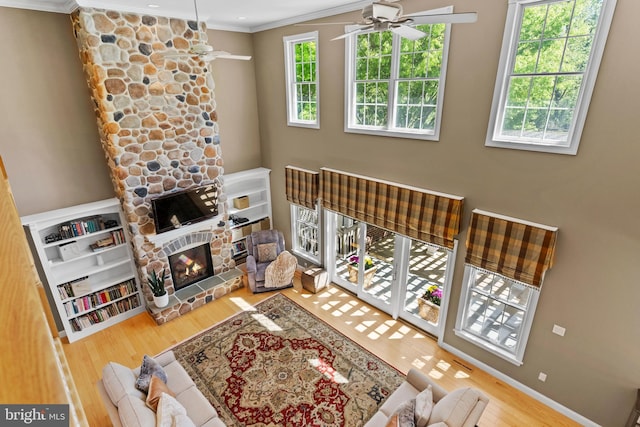 living area featuring a stone fireplace, ornamental molding, ceiling fan, and wood finished floors