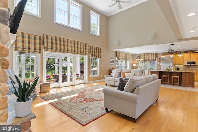 living room with crown molding, ceiling fan with notable chandelier, a high ceiling, recessed lighting, and light wood-style flooring