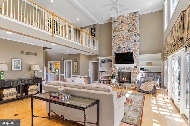 living area with a ceiling fan, visible vents, crown molding, a towering ceiling, and wood finished floors