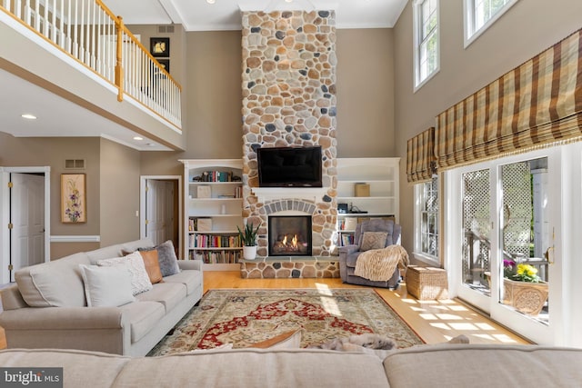 living room featuring wood finished floors, visible vents, a stone fireplace, and a towering ceiling