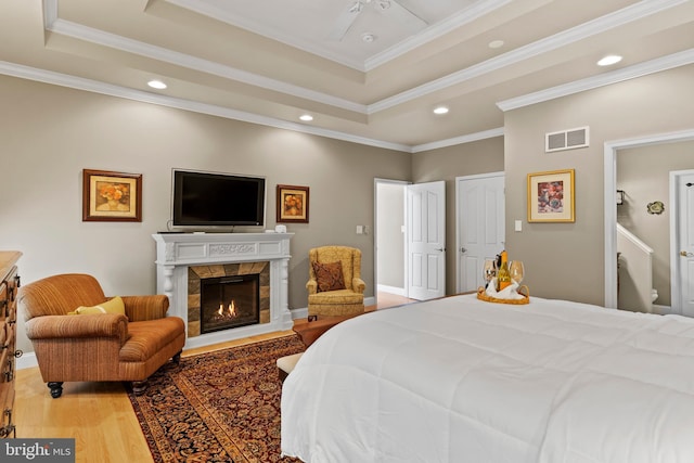 bedroom featuring visible vents, light wood-style flooring, a raised ceiling, and a tile fireplace