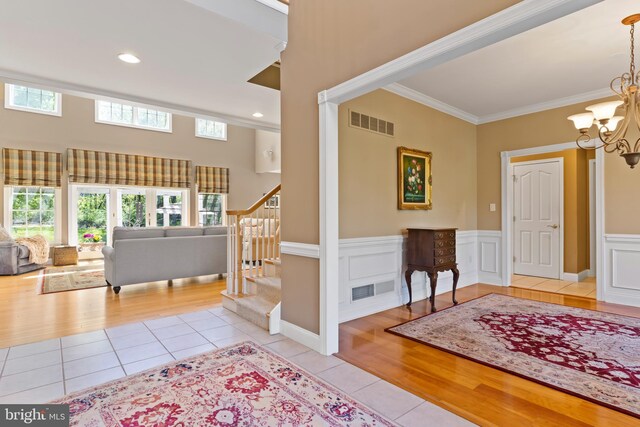 entrance foyer with tile patterned flooring, ornamental molding, stairs, visible vents, and an inviting chandelier