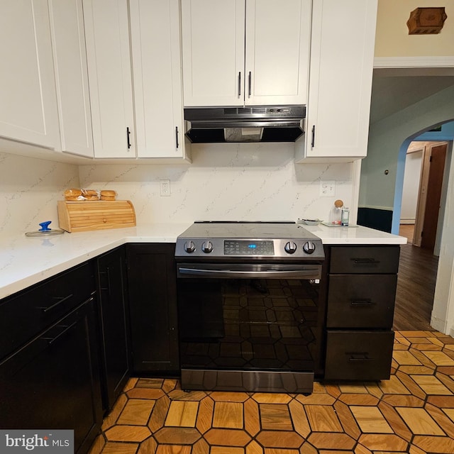 kitchen featuring electric range, under cabinet range hood, arched walkways, white cabinets, and tasteful backsplash