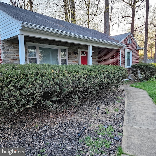 doorway to property featuring brick siding and roof with shingles