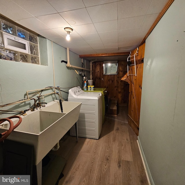 clothes washing area featuring light wood-style floors, washer and clothes dryer, baseboards, and wood walls