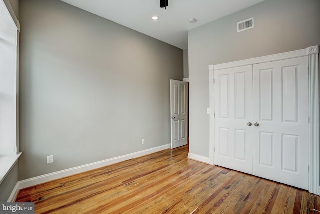 unfurnished bedroom featuring baseboards, a closet, visible vents, and wood finished floors