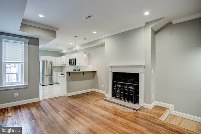 unfurnished living room featuring baseboards, ornamental molding, visible vents, and light wood-style floors