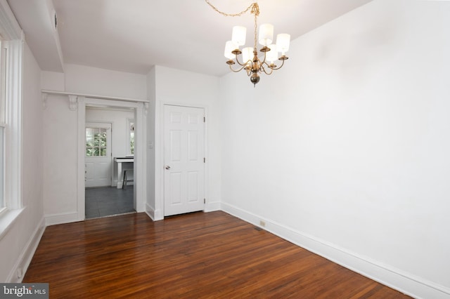 empty room featuring baseboards, an inviting chandelier, and dark wood-type flooring
