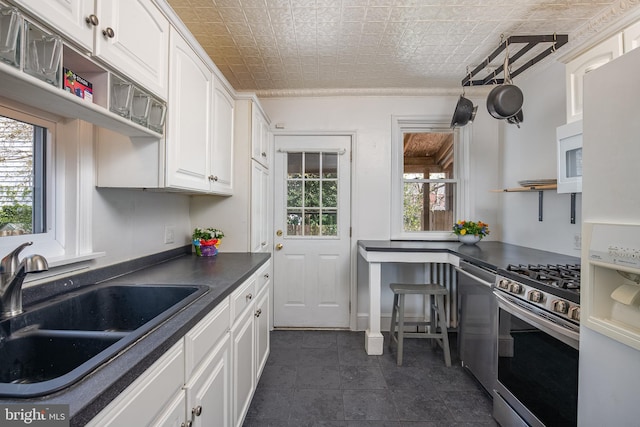 kitchen featuring a healthy amount of sunlight, open shelves, appliances with stainless steel finishes, dark countertops, and a sink