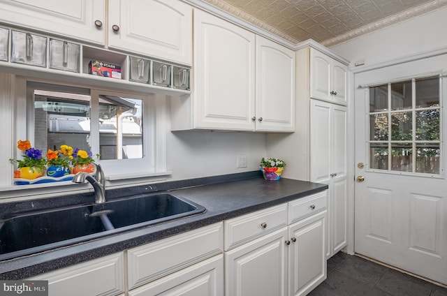 kitchen featuring dark tile patterned flooring, dark countertops, an ornate ceiling, white cabinetry, and a sink