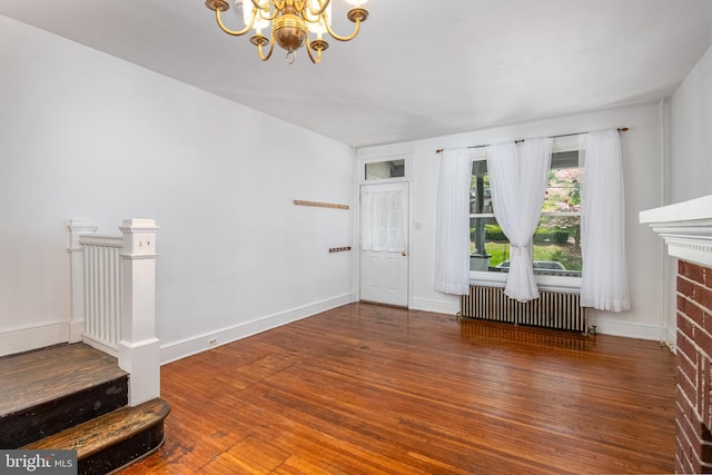 unfurnished living room with radiator heating unit, a notable chandelier, and wood-type flooring