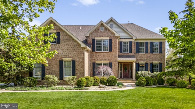 colonial inspired home featuring brick siding, a shingled roof, and a front yard