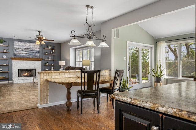 dining room with visible vents, a stone fireplace, built in shelves, a ceiling fan, and vaulted ceiling
