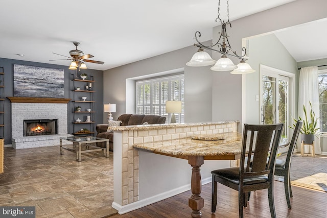 dining space with a brick fireplace, ceiling fan, and vaulted ceiling