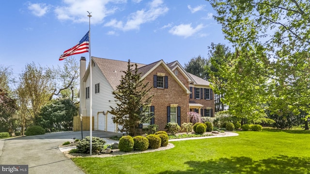 view of front of property featuring driveway, a chimney, a garage, brick siding, and a front lawn