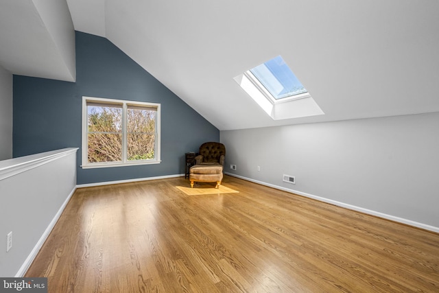 additional living space featuring baseboards, visible vents, wood finished floors, and vaulted ceiling with skylight