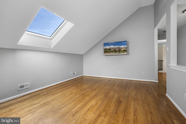 additional living space with baseboards, lofted ceiling with skylight, wood finished floors, and visible vents