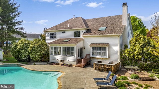 rear view of house featuring an outdoor pool, a chimney, outdoor dry bar, a shingled roof, and a patio area