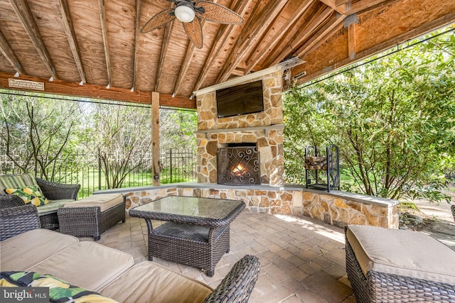 view of patio / terrace with fence, a ceiling fan, and an outdoor living space with a fireplace