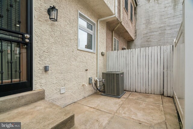 view of side of home with stucco siding, fence, entry steps, and central AC unit
