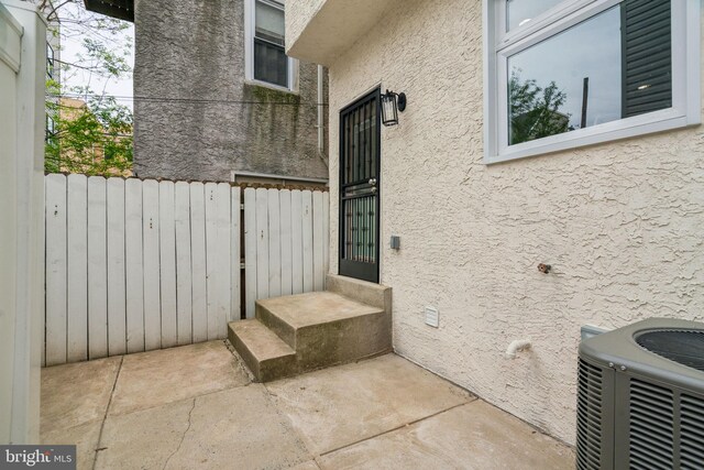 entrance to property featuring central AC unit, stucco siding, and fence