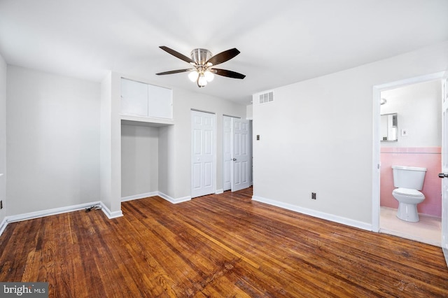 unfurnished bedroom with dark wood finished floors, visible vents, baseboards, and multiple closets