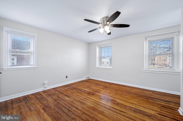 empty room with wood finished floors, visible vents, and baseboards