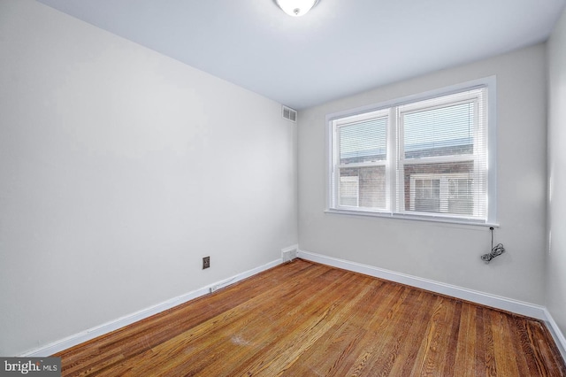 unfurnished room with baseboards, wood finished floors, and visible vents