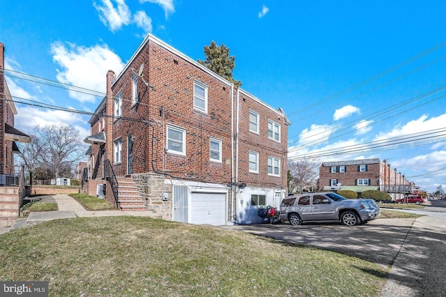 view of side of home with driveway, brick siding, a yard, and a garage