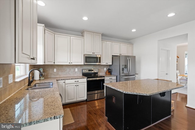 kitchen with stainless steel appliances, a sink, decorative backsplash, light stone counters, and a kitchen island
